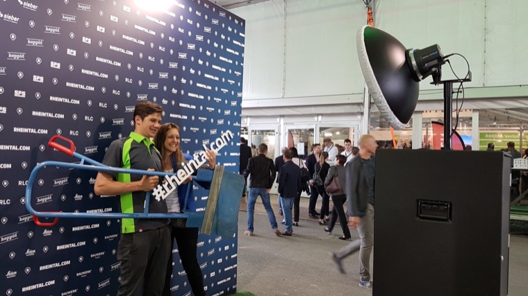 Besucher mit Hashtag-Schild vor der Fotobox am Messestand der RHEMA