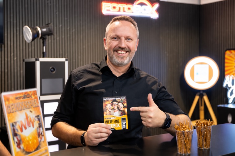 Freundlicher Ansprechpartner von FotoBox.ch am Messestand mit Flyer in der Hand